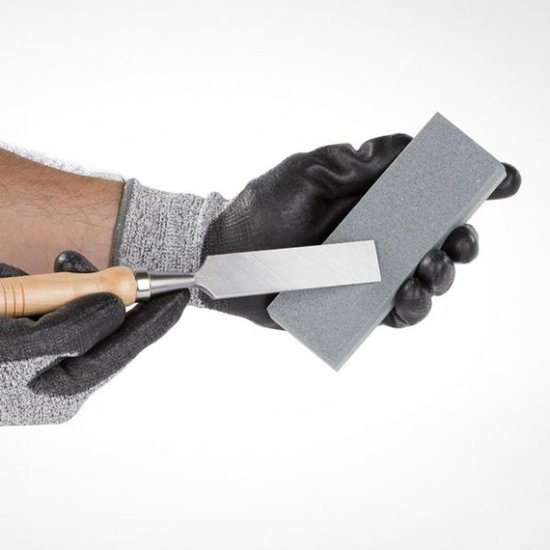 Handen met werkhandschoenen die een beitel slijpen op een grijze Kreator slijpsteen.