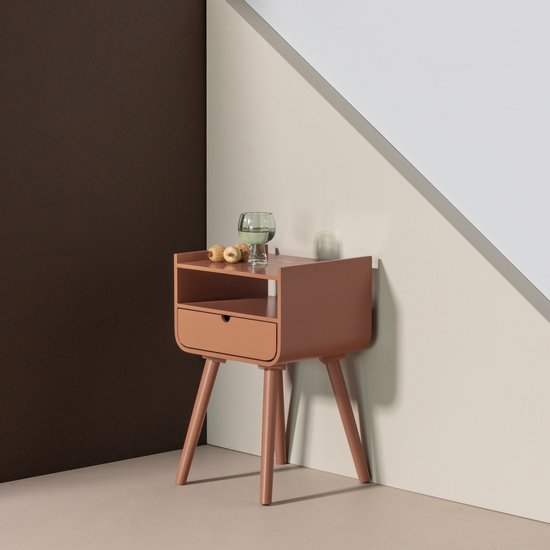 Oudroze bijzettafel met een open vak en een lade, op schuine pootjes, met een glas en decoratie.