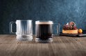 Glazen bierpul gevuld met donker bier en een lege bijpassende pul met verticale ribbels en decoratieve bodem.
