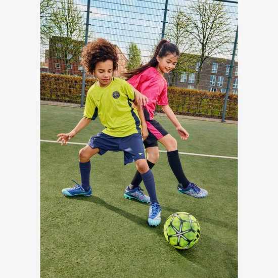 Twee kinderen in voetbalkleding op een groen veld, met een bal. Een jongen in geel/blauw, een meisje in roze/zwart.