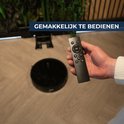 Hand houdt afstandsbediening bij zwarte robotstofzuiger op houten vloer.