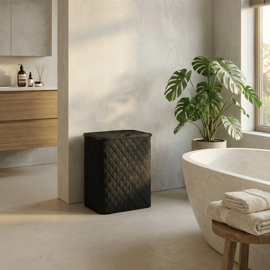 Zwarte gewatteerde wasmand met deksel in een badkamer, naast een badkuip en een plant.