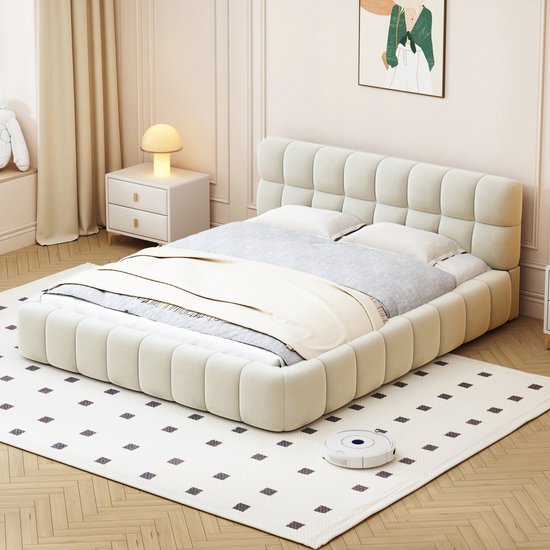 Lit double rembourré couleur crème avec tête de lit capitonnée, fait avec de la literie grise, sur un tapis à motifs de losanges.