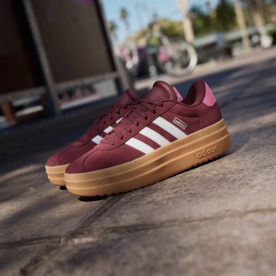Bordeauxrode Adidas sneakers met witte strepen en dikke gum-zolen, buiten.