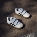 Twee witte sneakers met zwarte strepen, klittenbandsluiting en bruine zool, schuin van bovenaf.