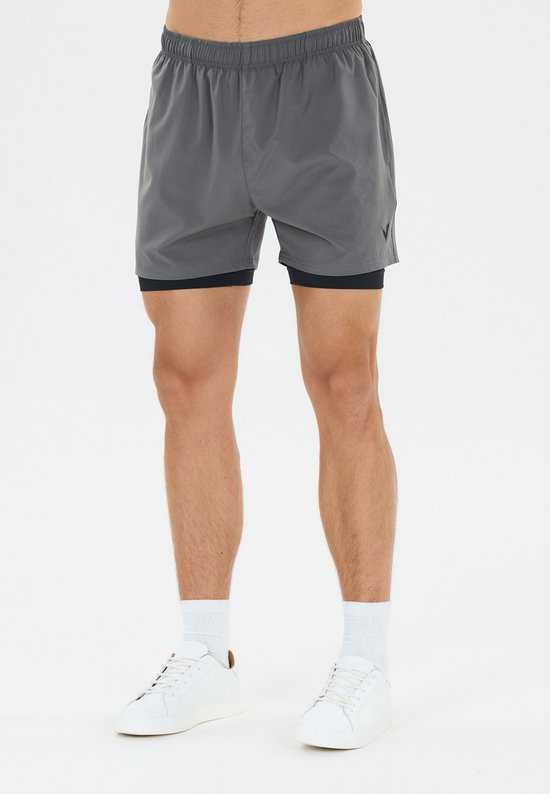 Man in grijze 2-in-1 sportbroek en blauw T-shirt, witte sneakers en sokken.