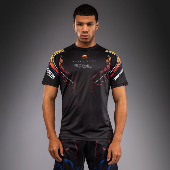 Zwart Venum x Tekken T-shirt met oranje, gele en blauwe grafische details op de schouders en rode lijnen op de borst. Het shirt heeft een ronde hals en korte mouwen.