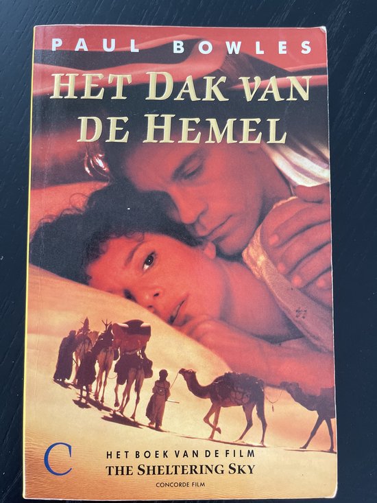 Boekomslag van "Het dak van de hemel" van Paul Bowles. Twee mensen omhelzen elkaar. Op de achtergrond een woestijnlandschap met kamelen en figuren.