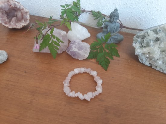 Roze kwarts armbandje op een houten ondergrond met mineralen en een Boeddhabeeldje.