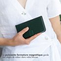 Close-up van een persoon met een witte top die een donkergroene boekhoes vasthoudt met de tekst 'La puissante fermeture magnétique garde vos objets de valeur dans votre housse'.