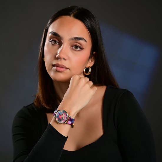 Model met een goudkleurig horloge om de pols, veelkleurige wijzerplaat en band.