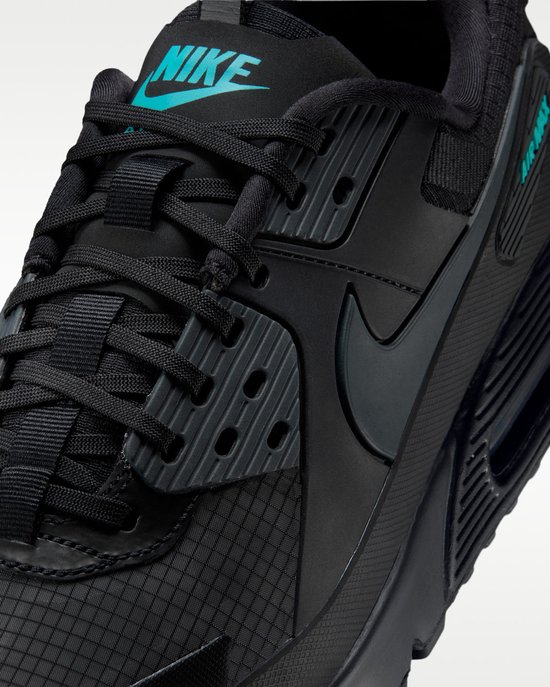 Close-up van de zwarte Nike Air Max 90 Drift sneaker met turquoise Nike Air logo op de tong en veters.