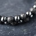 Gedetailleerde close-up van een dubbele armband met donkere, ruwe lavastenen en gladde, glanzende grijze kralen.