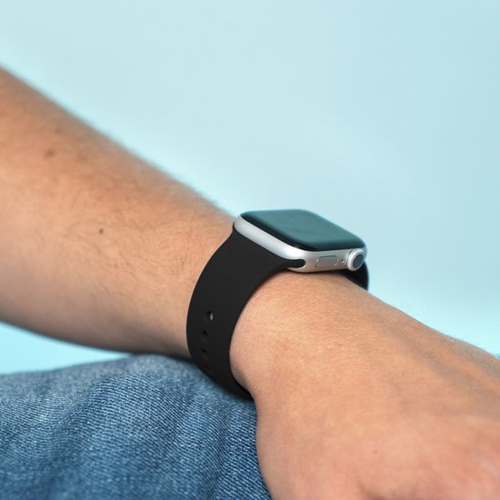 Zwarte imoshion smartwatchband om pols met zilverkleurig horloge en spijkerbroek.