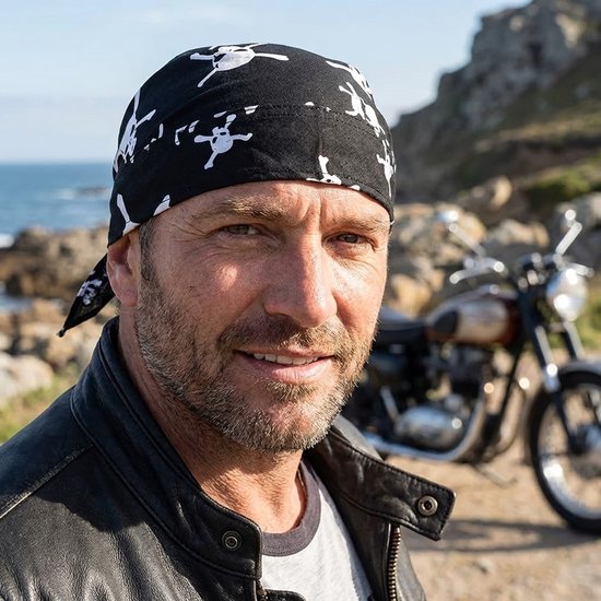 Zwart bandana met witte doodshoofdprint, gedragen door een man. Motor op de achtergrond.