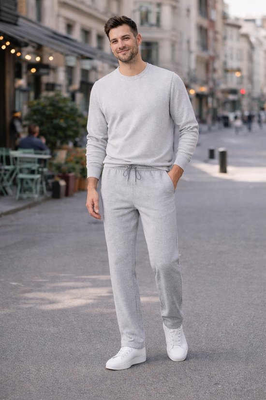 Man draagt grijze joggingbroek en lichtgrijze trui met ritskraag, witte sneakers in stad.