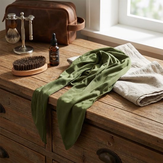 Groene bandana met mesh-structuur uitgevouwen op een houten ladekast, met scheerspullen en baardolie.
