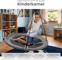 Jongen in grijze nestschommel met zwarte touwen, zittend in een kinderkamer.