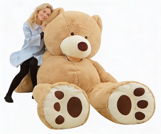 Een blonde vrouw in een lichtblauwe jas leunt tegen een grote bruine teddybeer, met de nadruk op de grote poten van de beer.