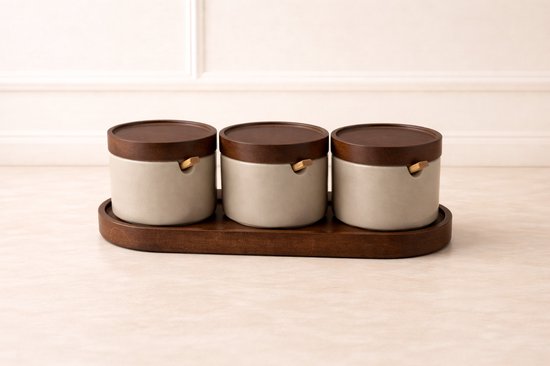 Trois pots beiges en céramique avec couvercles et cuillères en bois, sur un plateau en bois.