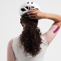 Vrouw draagt witte Rogelli fietshelm en witte trui met roze mesh mouwen. Achteraanzicht.
