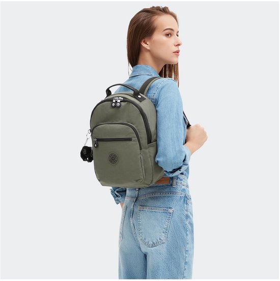 Vrouw met een denim blouse en jeans, draagt een legergroene Kipling rugzak.
