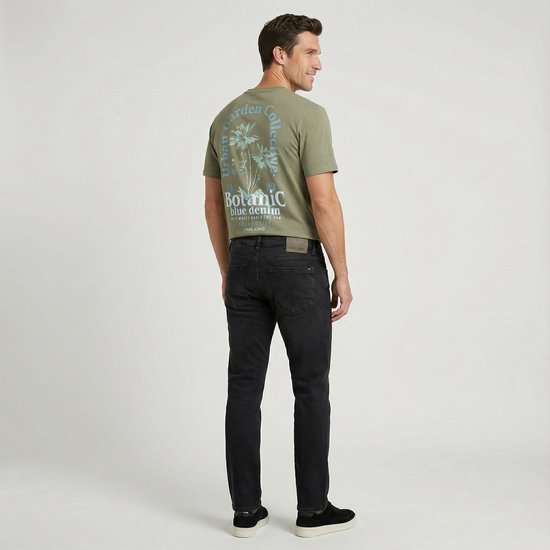 Man in olijfgroen Cars Jeans T-shirt met blauwe print op de rug en zwarte jeans.