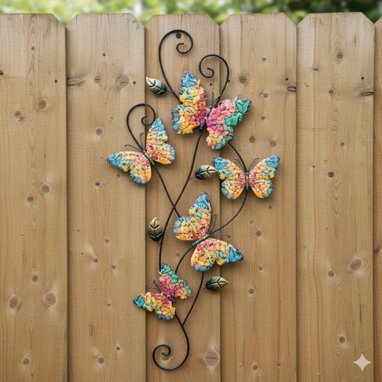 Gekleurde metalen vlinderdecoratie met vijf vlinders aan een metalen tak, gemonteerd op een houten schutting.