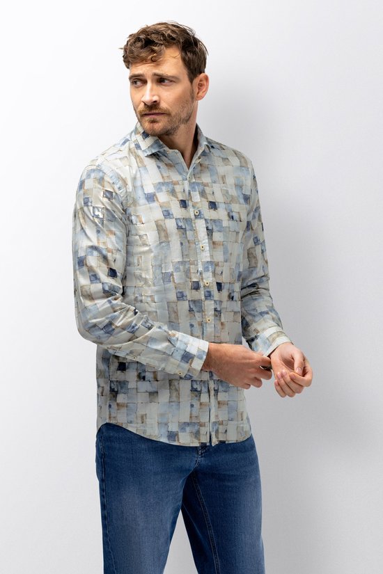 Man met donker haar, baard en snor, draagt een blauw-bruin blokkerig overhemd en spijkerbroek, mouwen oprollend.