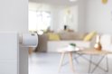 Een witte Netatmo slimme radiatorthermostaat met oranje accent, gemonteerd op een radiator in een woonkamer.