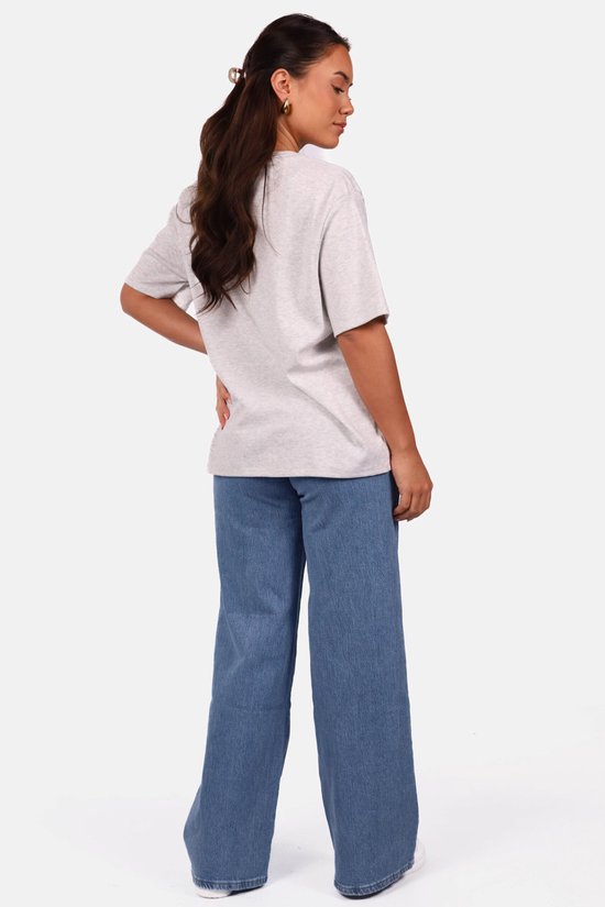 Model met de rug naar de camera in een lichtgrijs, oversized T-shirt en jeans.