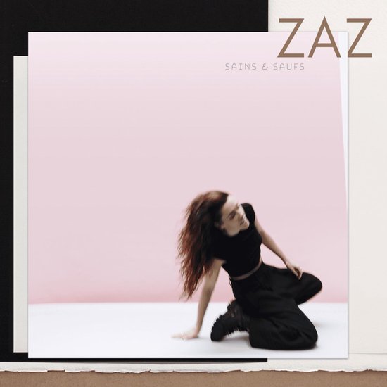 Zaz in zwart topje en broek, met wapperend haar, zittend op de grond.