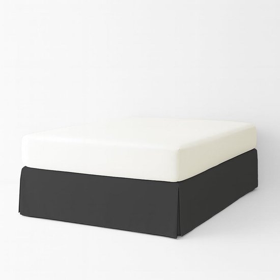 Donkergrijze bedrok met plooien, bedekt een witte matras die rust op een metalen frame.
