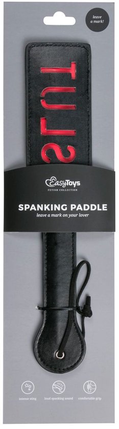 Zwarte spanking paddle van leer met rode tekst "SLUT" op de kop, in verpakking.