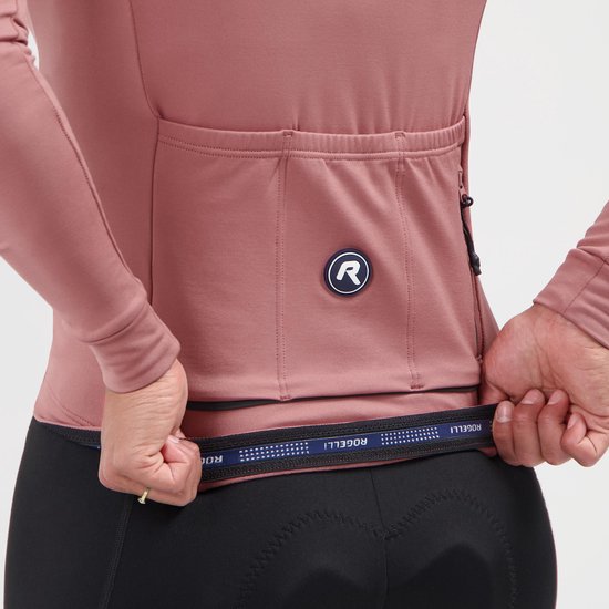 Close-up van de achterkant van een oudroze fietsshirt, waar de zakken en de elastische tailleband met logo zichtbaar zijn.