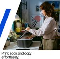 Jonge vrouw met roze trui opent de scannerklep van een zwarte HP DeskJet printer.