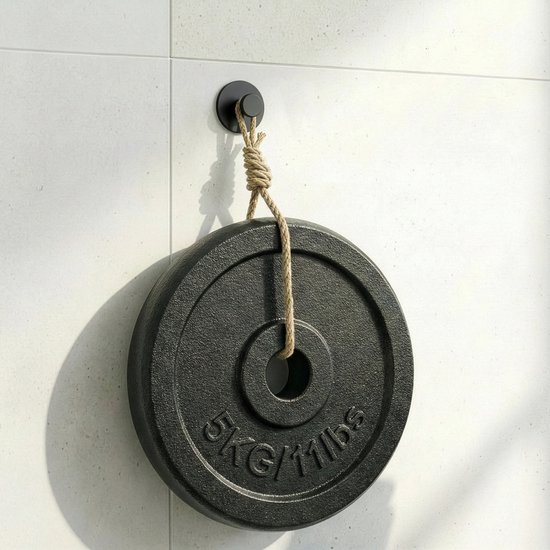 Zwarte ronde haak aan een betegelde muur, draagt een zware schijf van 5kg.
