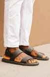 Donkergroene sandalen met twee banden en een gesp, gedragen door een persoon met een witte broek.