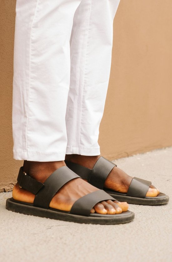 Donkergroene sandalen met twee banden en een gesp, gedragen door een persoon met een witte broek.