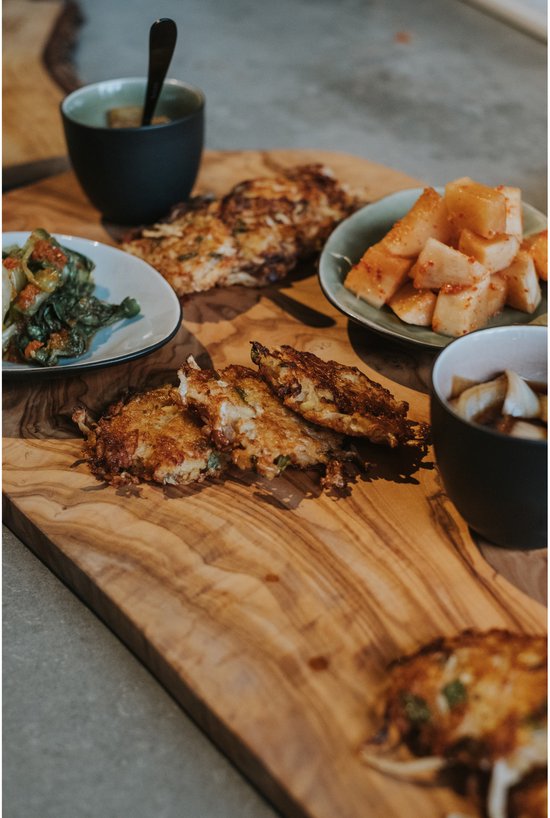 Houten plank met diverse Koreaanse bijgerechten: pannenkoekjes, kimchi en andere groenten.