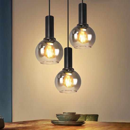 Trois suspensions avec sphères en verre fumé et douilles métalliques noires au-dessus d'une table en bois.