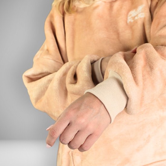 Close-up van de mouw van een oversized beige hoodie deken die door een vrouw wordt gedragen. De manchet is van geribd beige materiaal.