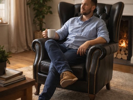 Man zittend in een zwarte leren wingback fauteuil met capitons.