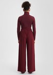Achterkant: model draagt een bordeauxrode coltrui en een bordeauxrode wijde broek met elastische taille.