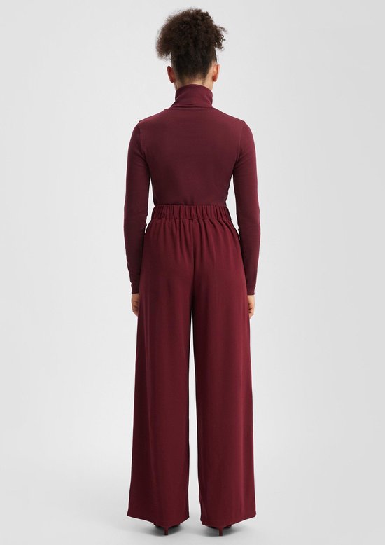 Achterkant: model draagt een bordeauxrode coltrui en een bordeauxrode wijde broek met elastische taille.