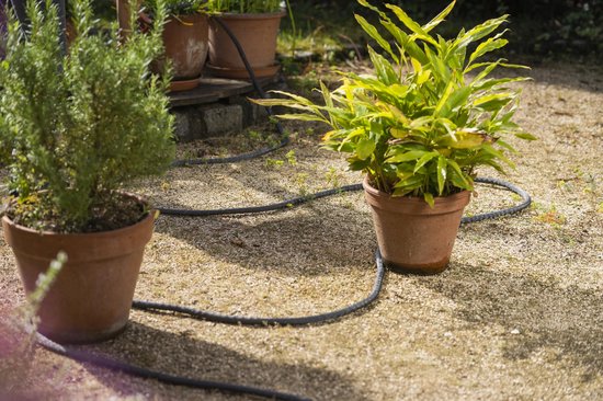 Grijze Gardena Liano Life tuinslang ligt op grindpad tussen plantenpotten.
