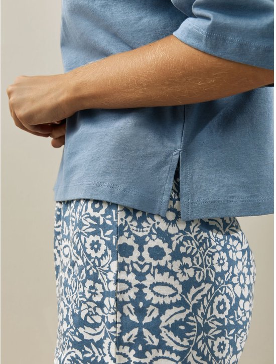 Detail van blauw t-shirt met split aan de zijkant over een korte pyjamabroek met bloemenprint.