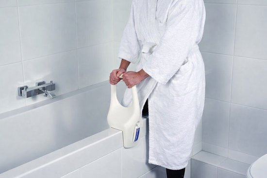 Een persoon met een witte badjas gebruikt een witte badrandbeugel om in de badkuip te stappen.