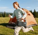Donkergrijs Jackery Explorer 500 draagbaar powerstation met oranje accenten, in de hand van een rennend meisje, bij een tent.