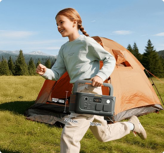 Donkergrijs Jackery Explorer 500 draagbaar powerstation met oranje accenten, in de hand van een rennend meisje, bij een tent.
